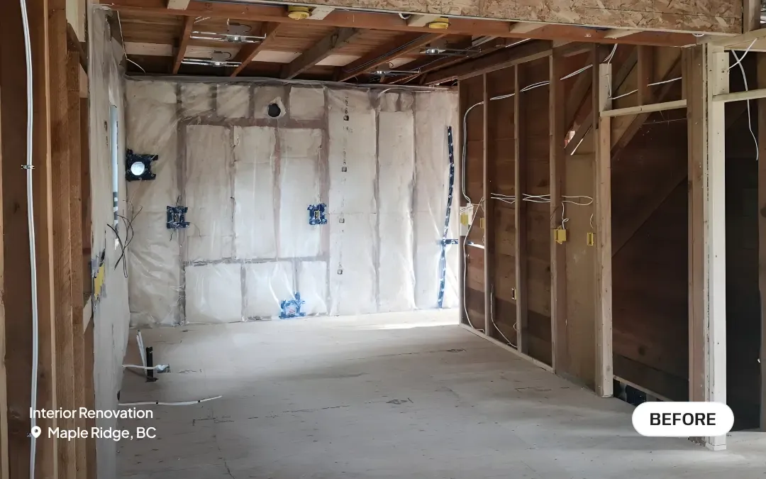 A before photo of an interior renovation in Maple Ridge, BC, showing a space completely stripped down to the wooden wall studs and ceiling joists, with exposed insulation and rough-in electrical wiring by PCC Renovations.